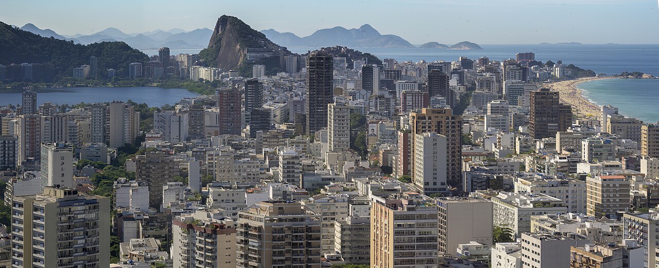 Vista panorâmica do Rio de Janeiro, com edifícios, montanhas, lagoa e mar.